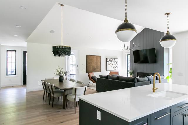 Bright open kitchen with a long quartz island, brass pendant lights and a vaulted great room beyond
